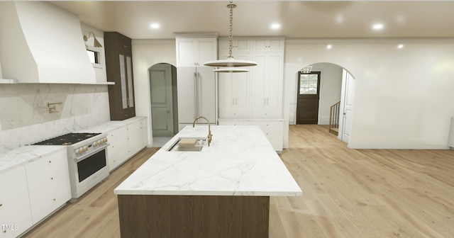 kitchen with white cabinetry, high end stove, a kitchen island with sink, and custom range hood