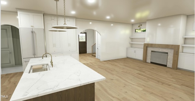 kitchen featuring a spacious island, sink, white cabinetry, high quality fridge, and light stone countertops