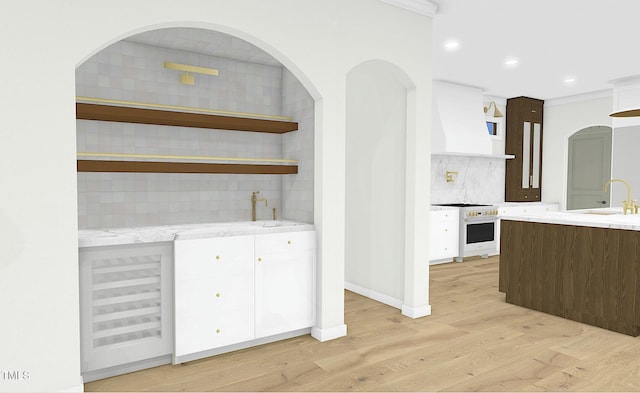 interior space featuring sink, light wood-type flooring, custom range hood, stove, and backsplash