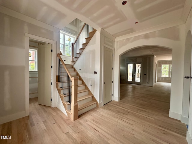 stairway featuring a healthy amount of sunlight, wood finished floors, baseboards, and arched walkways