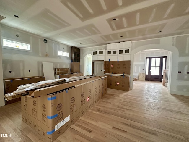 kitchen featuring arched walkways, light wood-style floors, a center island, and glass insert cabinets