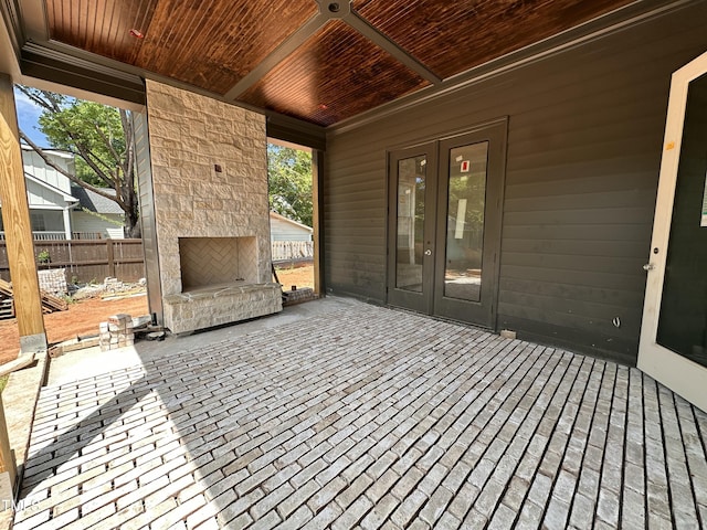 wooden terrace with an outdoor stone fireplace, french doors, fence, and a patio