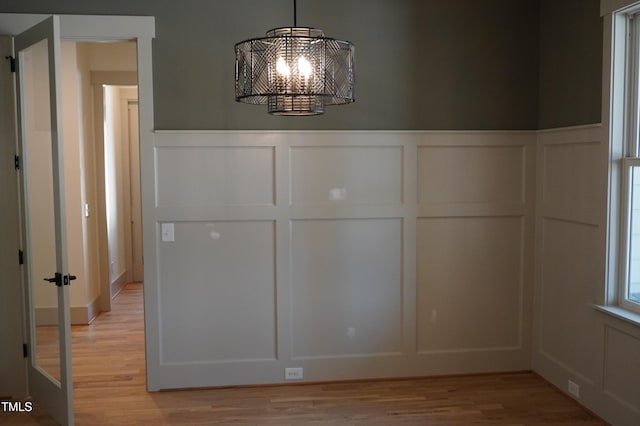 interior space featuring light wood-type flooring, a notable chandelier, and a decorative wall