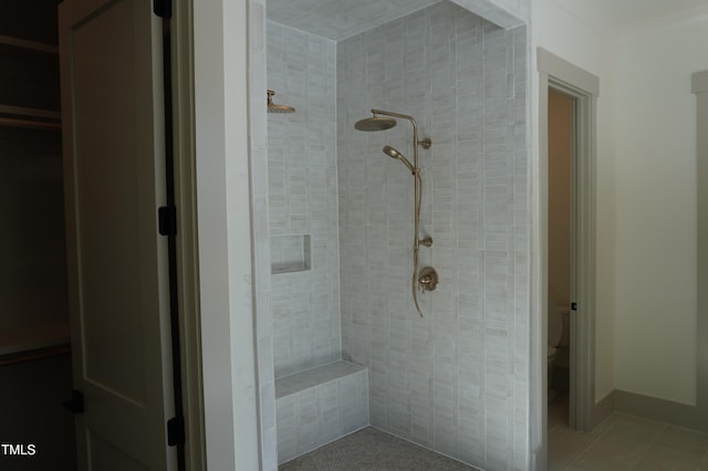 bathroom with a tile shower, toilet, and tile patterned floors