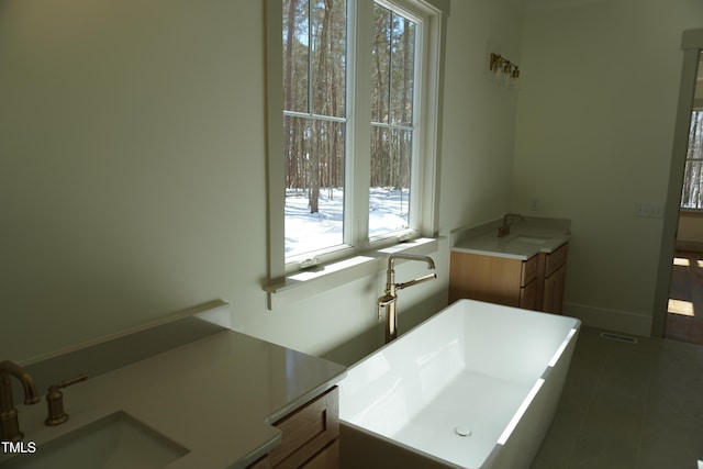 bathroom featuring visible vents, vanity, a freestanding tub, baseboards, and tile patterned floors