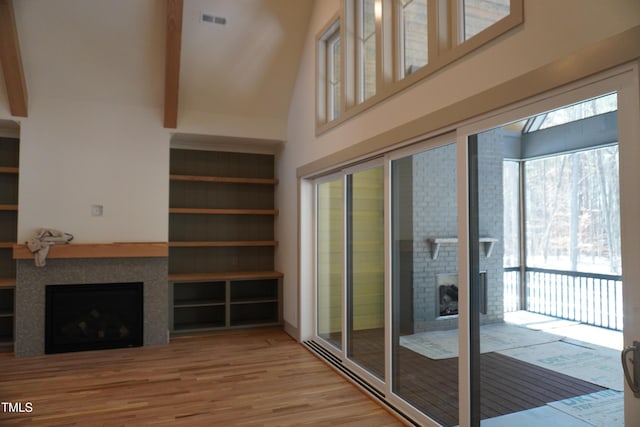 unfurnished living room featuring a fireplace, wood finished floors, a towering ceiling, visible vents, and beamed ceiling