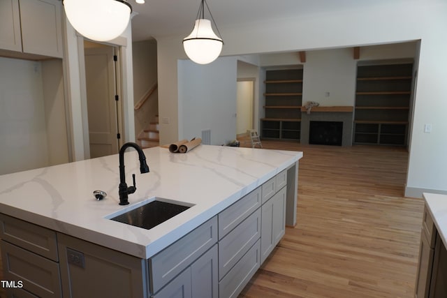 kitchen featuring hanging light fixtures, a sink, light stone countertops, and gray cabinetry