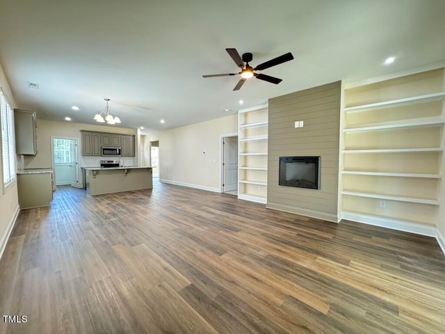 unfurnished living room with built in shelves, hardwood / wood-style flooring, ceiling fan with notable chandelier, and a large fireplace