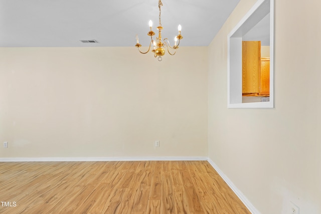 unfurnished room featuring an inviting chandelier and hardwood / wood-style flooring