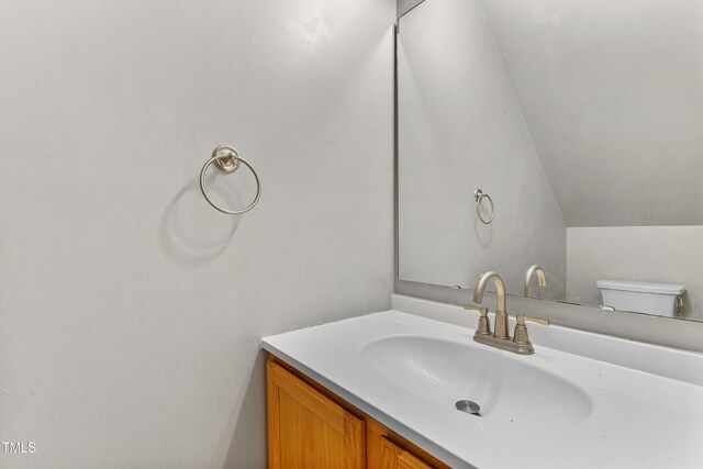 bathroom with vaulted ceiling, vanity, and toilet