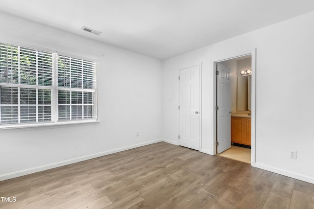 unfurnished bedroom with connected bathroom and hardwood / wood-style flooring