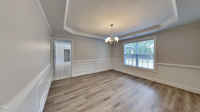 empty room with hardwood / wood-style flooring, a tray ceiling, and a chandelier