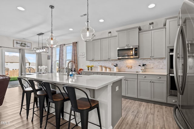 kitchen with hanging light fixtures, gray cabinets, light hardwood / wood-style flooring, and appliances with stainless steel finishes