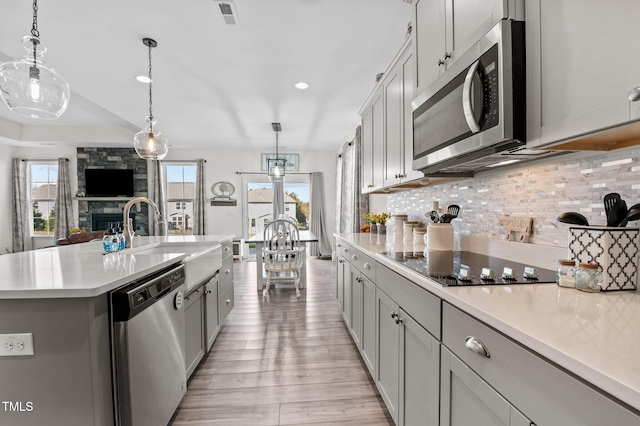 kitchen featuring appliances with stainless steel finishes, hanging light fixtures, sink, an island with sink, and light hardwood / wood-style floors