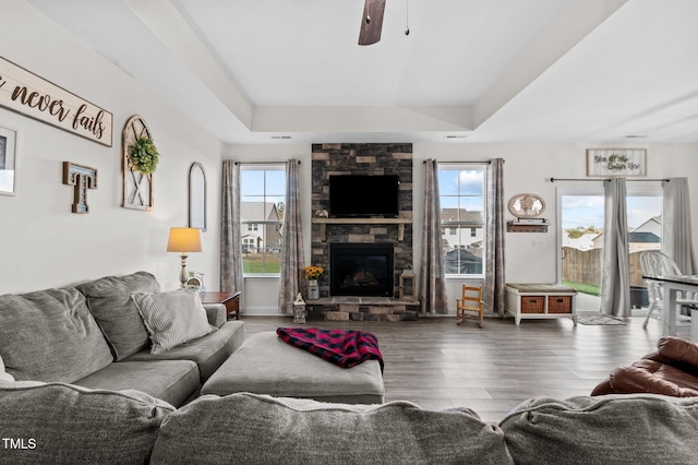 living room featuring ceiling fan, hardwood / wood-style flooring, a stone fireplace, and a raised ceiling