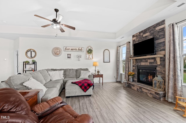 living room with plenty of natural light, a stone fireplace, ceiling fan, and light hardwood / wood-style flooring