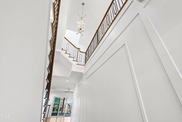 stairway with ceiling fan with notable chandelier and a high ceiling