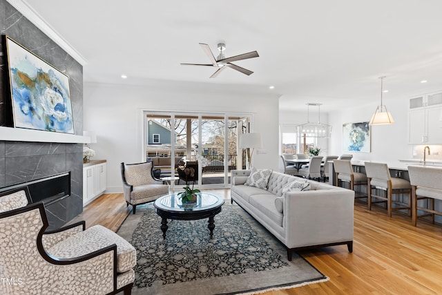 living room featuring ceiling fan, light hardwood / wood-style flooring, ornamental molding, and a fireplace