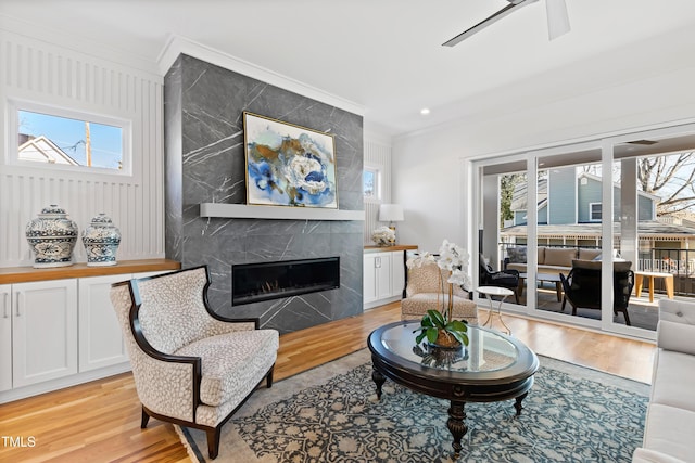 living room featuring ornamental molding, a premium fireplace, light wood-type flooring, and ceiling fan