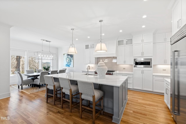 kitchen featuring sink, white cabinetry, pendant lighting, decorative backsplash, and a kitchen island with sink