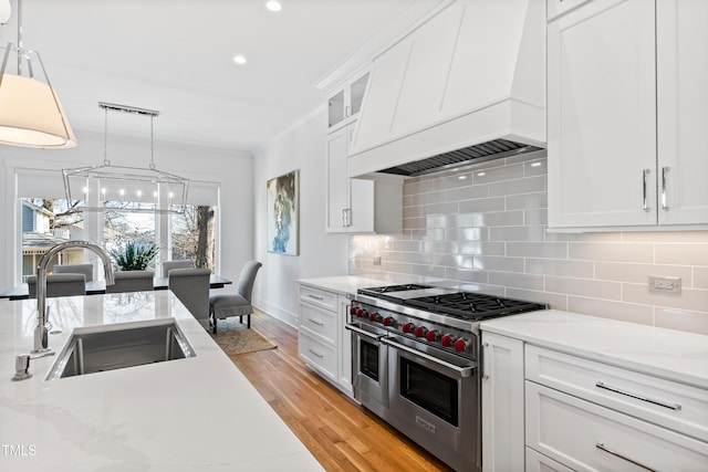 kitchen with sink, double oven range, white cabinetry, and custom range hood