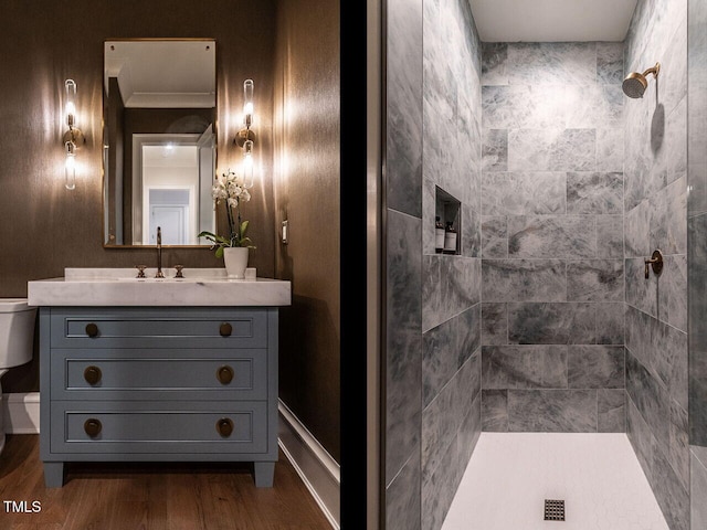 bathroom with ornamental molding, a tile shower, vanity, hardwood / wood-style flooring, and toilet