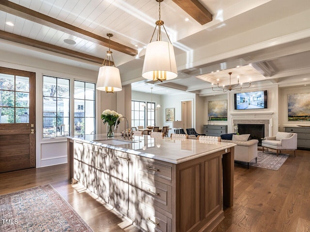 kitchen featuring dark wood-type flooring, sink, hanging light fixtures, an island with sink, and beamed ceiling