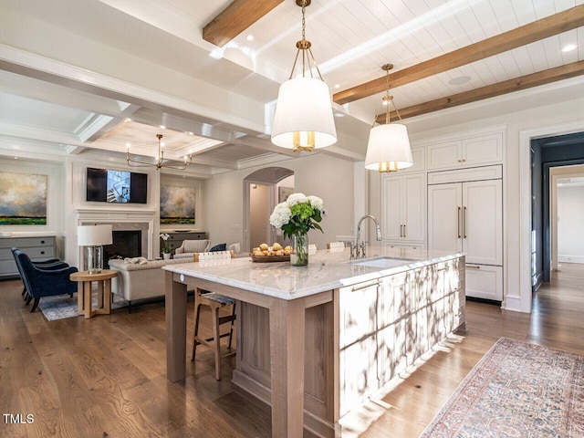 kitchen featuring light stone countertops, sink, beamed ceiling, decorative light fixtures, and a center island with sink