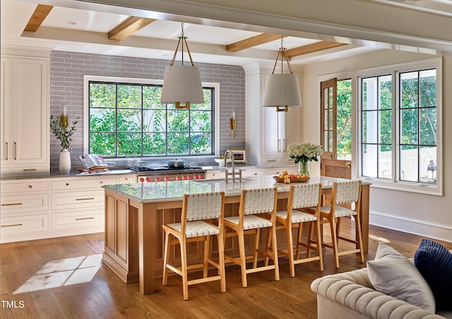1307 Mayfair Rd, Raleigh, NC 27608 - kitchen featuring beam ceiling, light stone counters, an island with sink, wood finished floors, and a kitchen breakfast bar