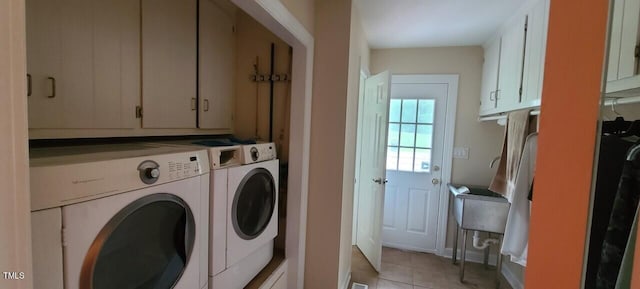 clothes washing area with washer and clothes dryer, cabinet space, and light tile patterned floors