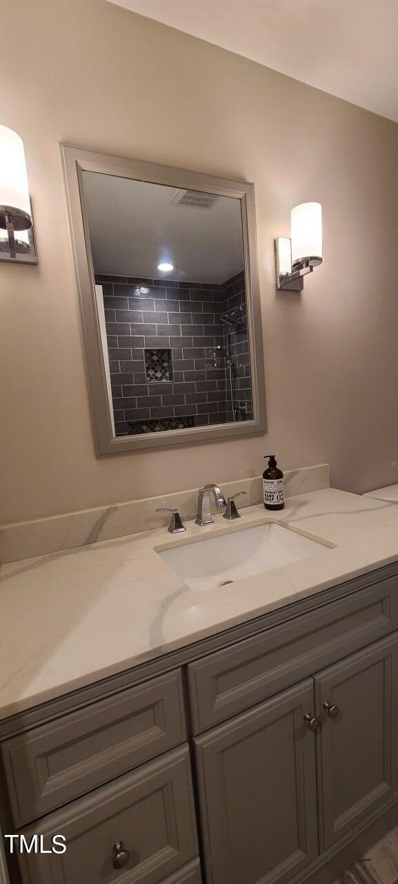 full bathroom with vanity, tiled shower, and visible vents