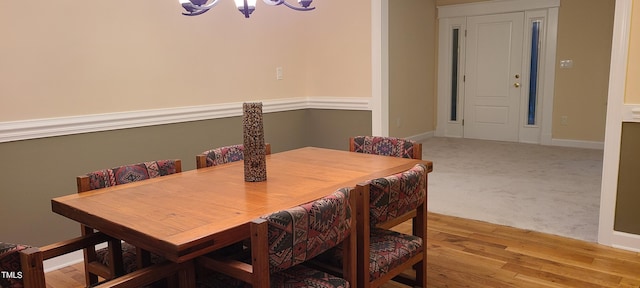 dining area featuring light wood finished floors, light colored carpet, a notable chandelier, and baseboards