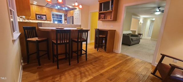 kitchen with a kitchen breakfast bar, open shelves, ceiling fan, light wood-style flooring, and appliances with stainless steel finishes