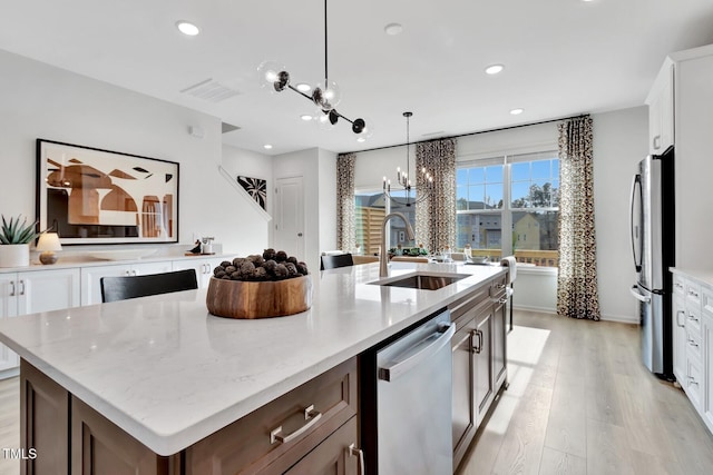 kitchen with white cabinets, hanging light fixtures, a kitchen island with sink, and stainless steel appliances