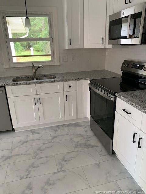 kitchen featuring appliances with stainless steel finishes, white cabinetry, pendant lighting, dark stone counters, and sink