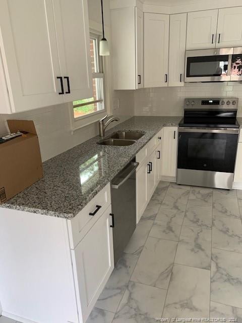 kitchen featuring white cabinets, backsplash, pendant lighting, stainless steel appliances, and sink