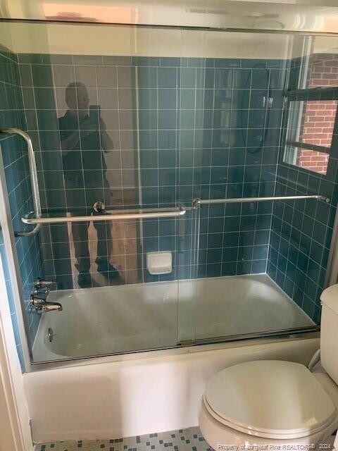 bathroom featuring combined bath / shower with glass door, toilet, and tile patterned floors