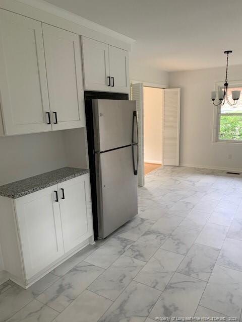 kitchen with pendant lighting, a notable chandelier, white cabinetry, stainless steel refrigerator, and dark stone countertops