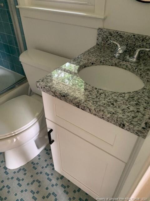 full bathroom featuring shower / bath combination with glass door, tile patterned flooring, vanity, and toilet