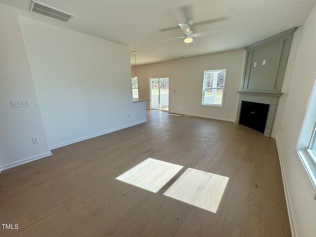 unfurnished living room with ceiling fan, a large fireplace, wood finished floors, visible vents, and baseboards