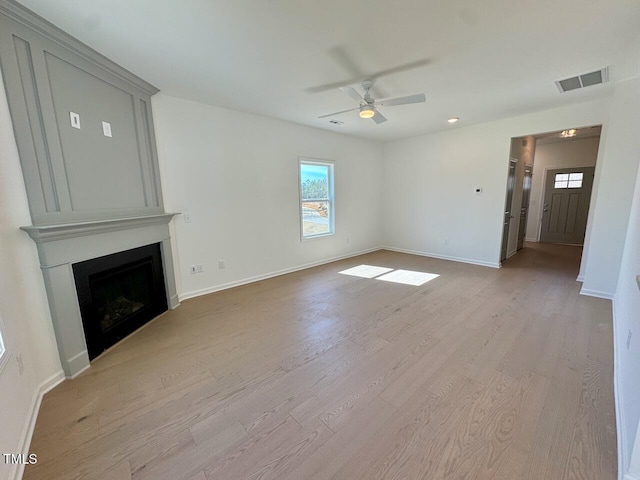 unfurnished living room featuring light wood-type flooring, a large fireplace, visible vents, and a wealth of natural light