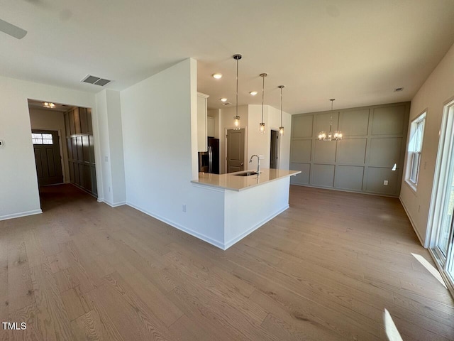 kitchen featuring a notable chandelier, light wood finished floors, light countertops, a sink, and refrigerator with ice dispenser