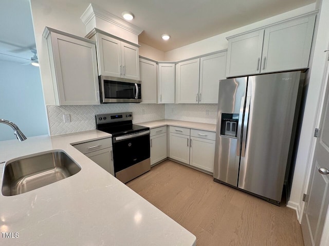 kitchen with appliances with stainless steel finishes, a sink, light countertops, light wood-type flooring, and backsplash