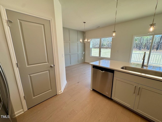 kitchen featuring light wood-style floors, pendant lighting, dishwasher, and a sink