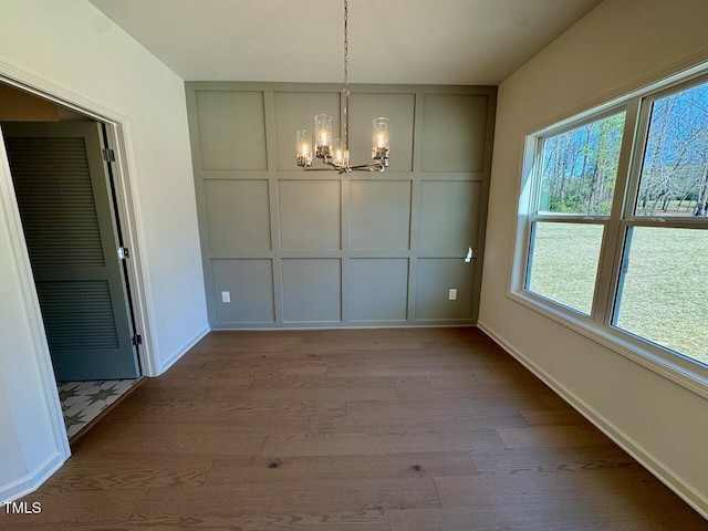 unfurnished dining area with a chandelier, baseboards, wood finished floors, and a decorative wall