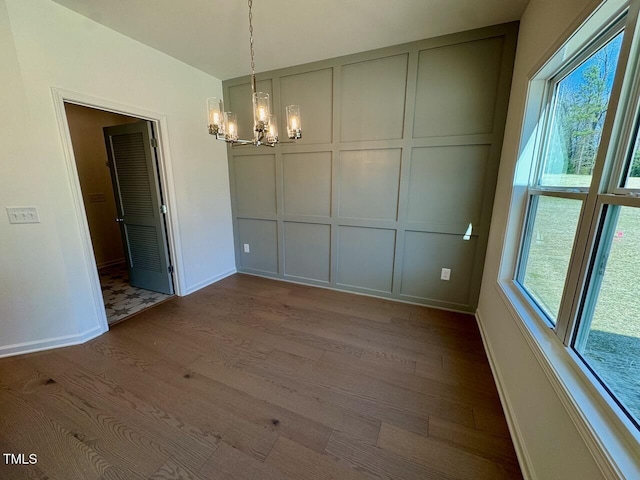 unfurnished dining area featuring a notable chandelier, baseboards, wood finished floors, and a decorative wall