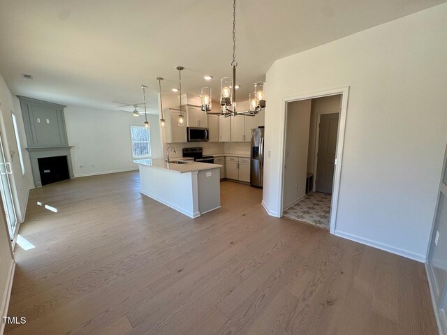 kitchen with a fireplace, light countertops, appliances with stainless steel finishes, open floor plan, and light wood-type flooring