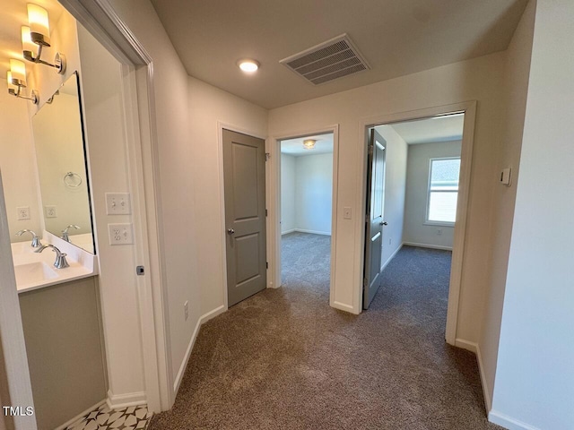 hall featuring dark colored carpet, visible vents, a sink, and baseboards