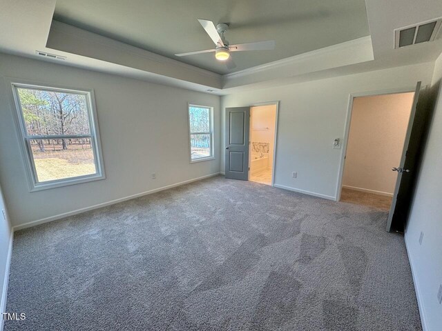 unfurnished bedroom featuring carpet floors, a tray ceiling, visible vents, and baseboards