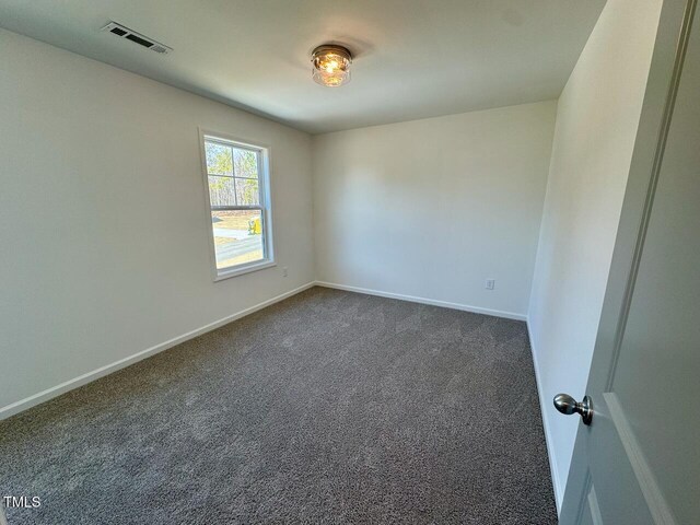 empty room with dark colored carpet, visible vents, and baseboards